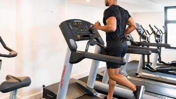 Un homme court sur un tapis de course dans une salle de sport équipée de plusieurs tapis de course et d’appareils d’exercice.