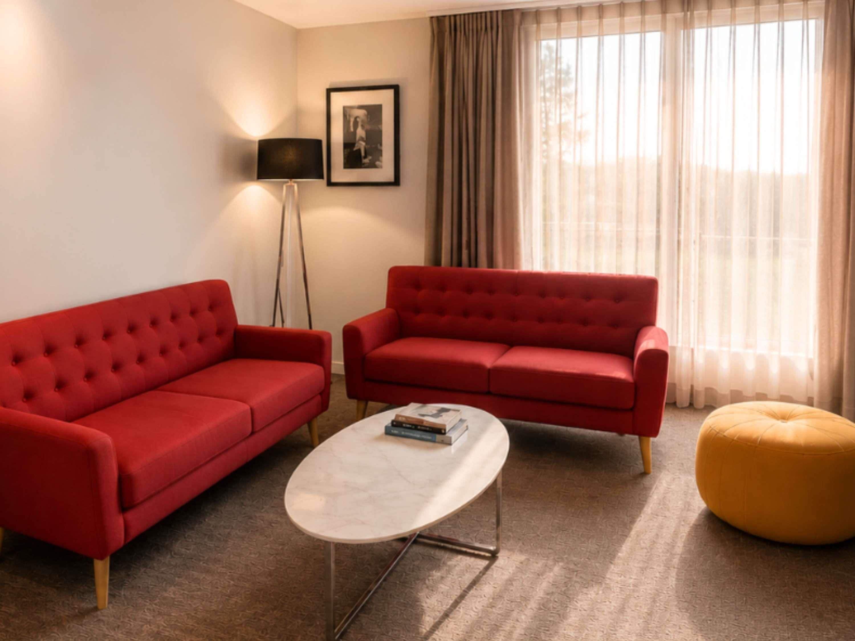 Una sala de estar con dos sofás rojos, una mesa de centro blanca y un otoman amarillo.