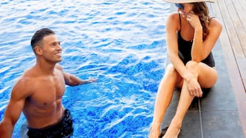 A man and a woman in a swimming pool with a wooden deck.