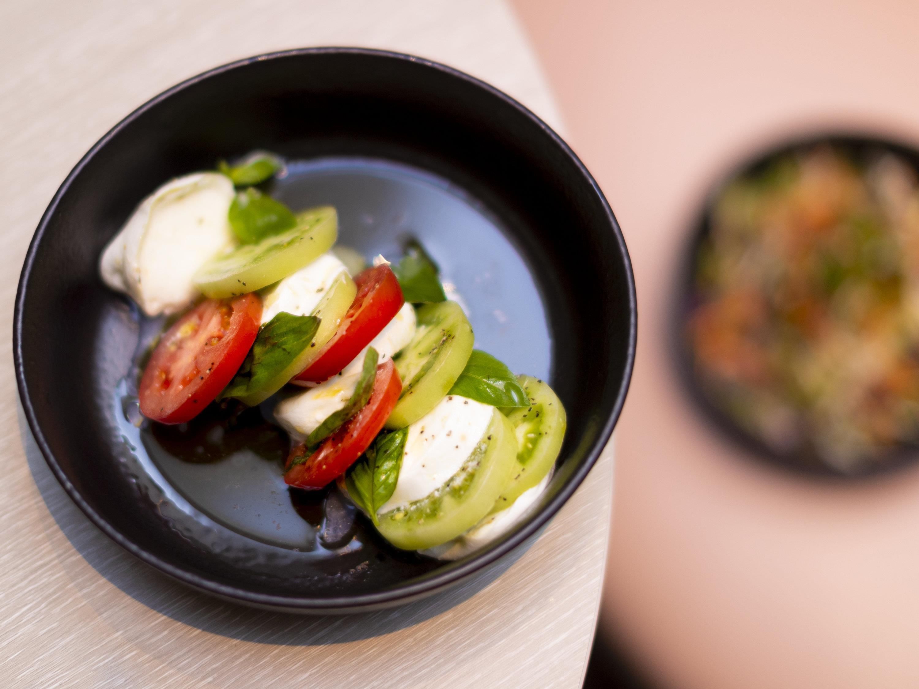 A black bowl with a salad of tomatoes, mozzarella, and basil on a wooden table.
