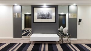 A hotel lobby with a framed cityscape photograph, a bench, and two vases on a glass table. - Novotel Sydney International Airport Hotel (Wolli Creek)