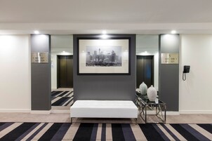 A hotel lobby with a framed cityscape photograph, a bench, and two vases on a glass table.