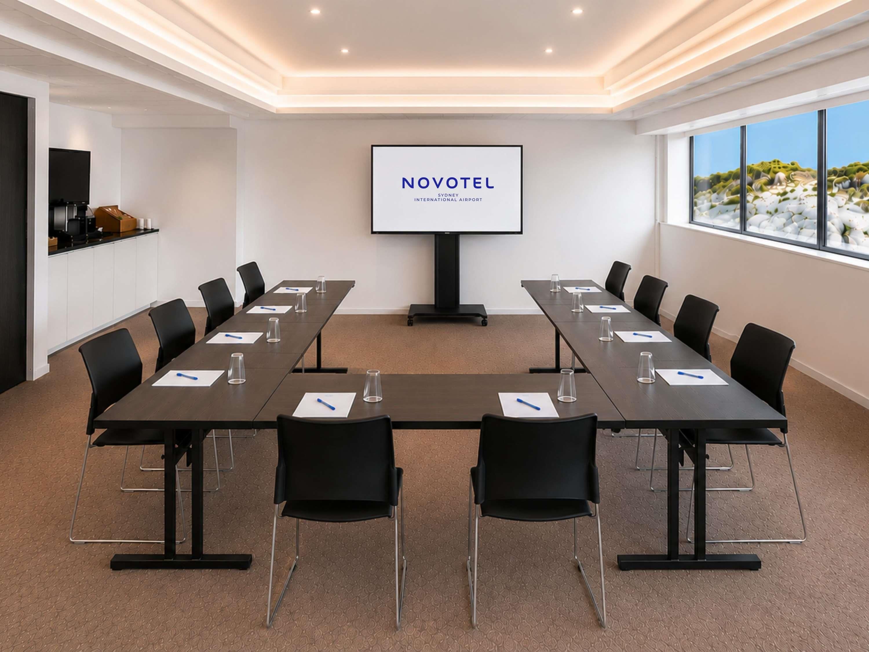 Une salle de conférence équipée d’une longue table, de chaises, d’un écran de projection et offrant une vue sur l’extérieur.