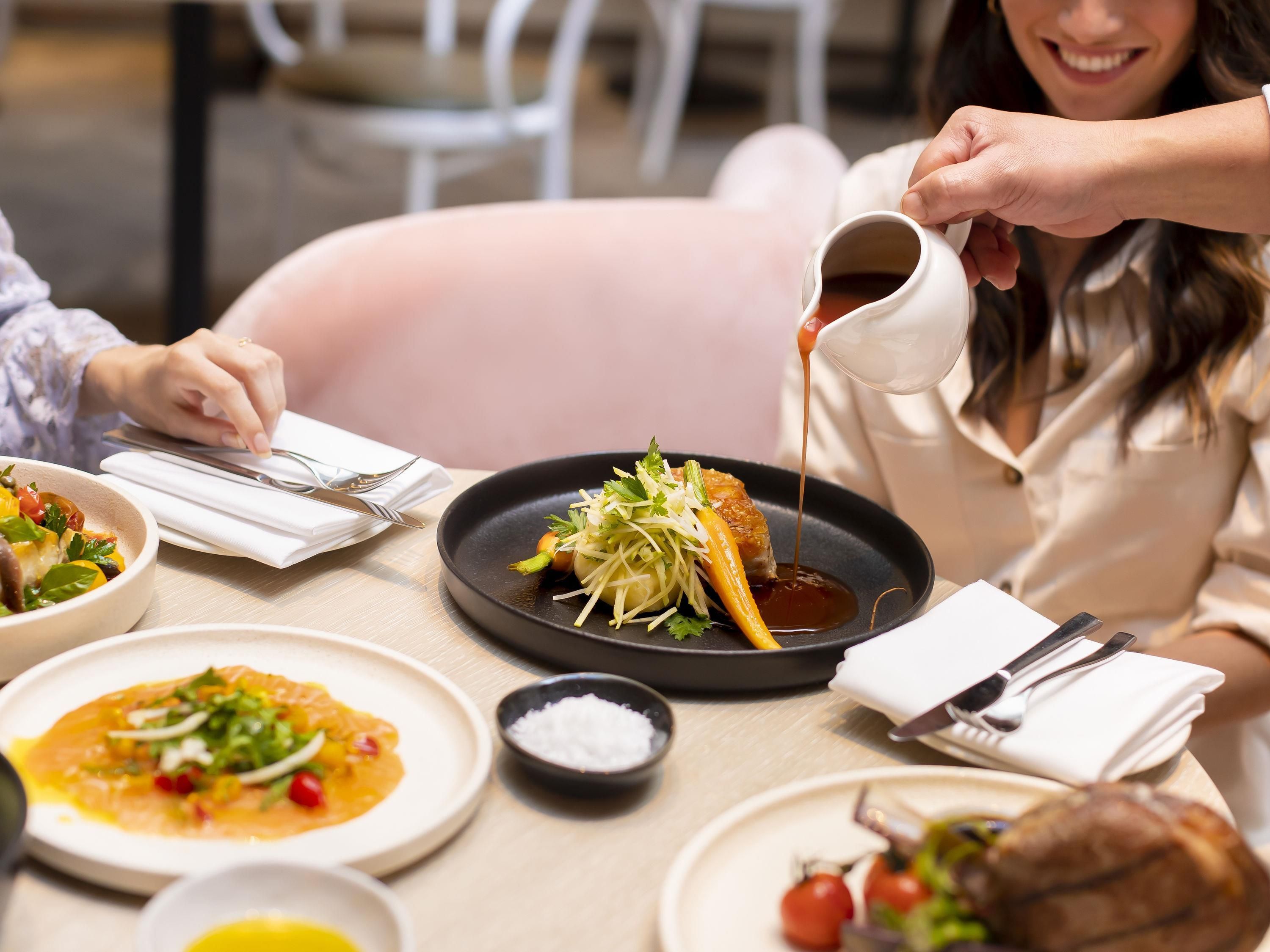 A dining table with various dishes, utensils, and a person pouring a liquid onto a plate.