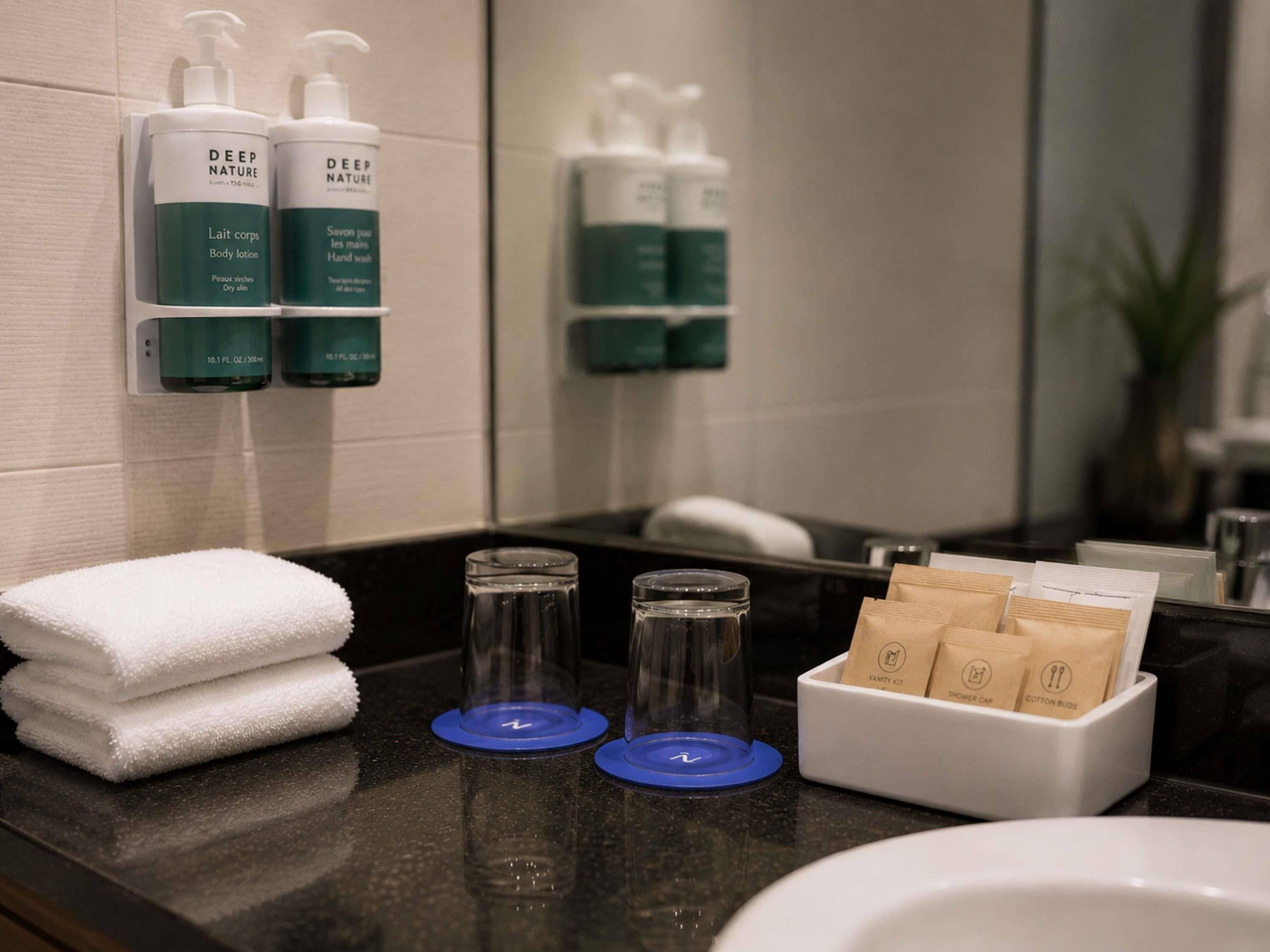 A bathroom with a sink, two bottles of body lotion, a stack of white towels, and a vanity kit with cotton buds.