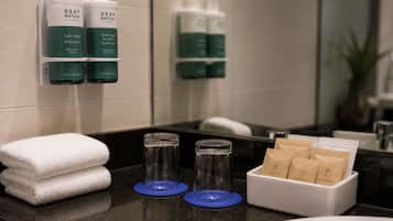 A bathroom with a sink, two bottles of body lotion, a stack of white towels, and a vanity kit with cotton buds.
