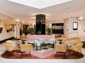 Un lobby moderno con una zona de estar central, un mostrador de recepción y un bar.