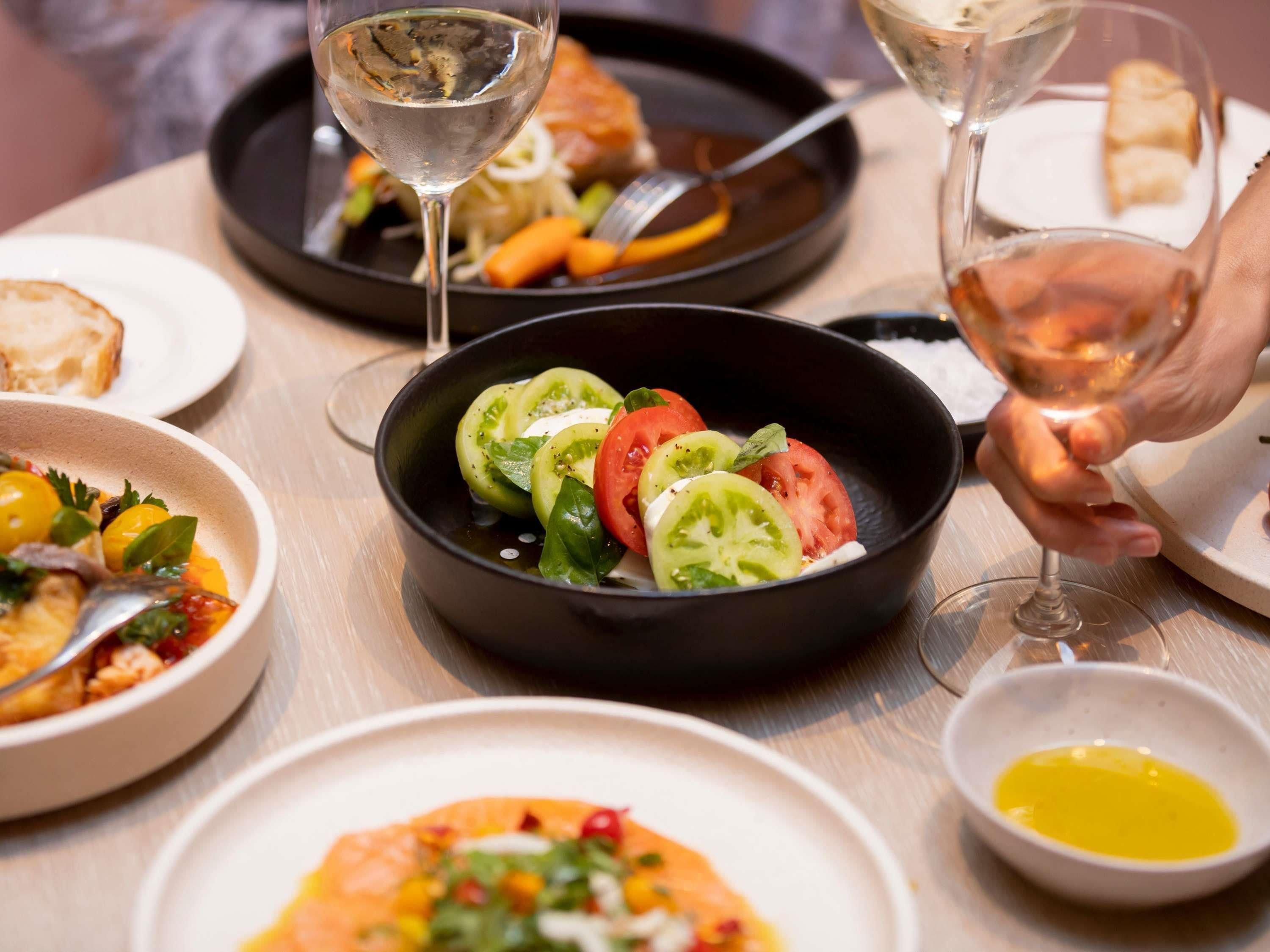 A dining table with various dishes, including a salad in a black bowl, a plate with bread, and a glass of white wine.