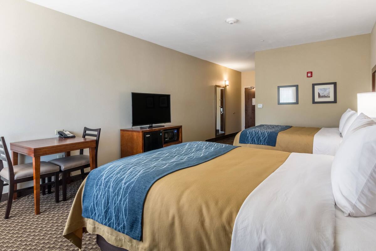 Une chambre d’hôtel avec deux lits, un bureau avec une chaise, une télévision et un mini-bar.