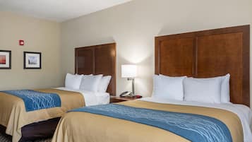 Habitación de hotel con dos camas, cubrecamas color beige y azul, una mesita de noche con lámpara y cuadros en la pared.