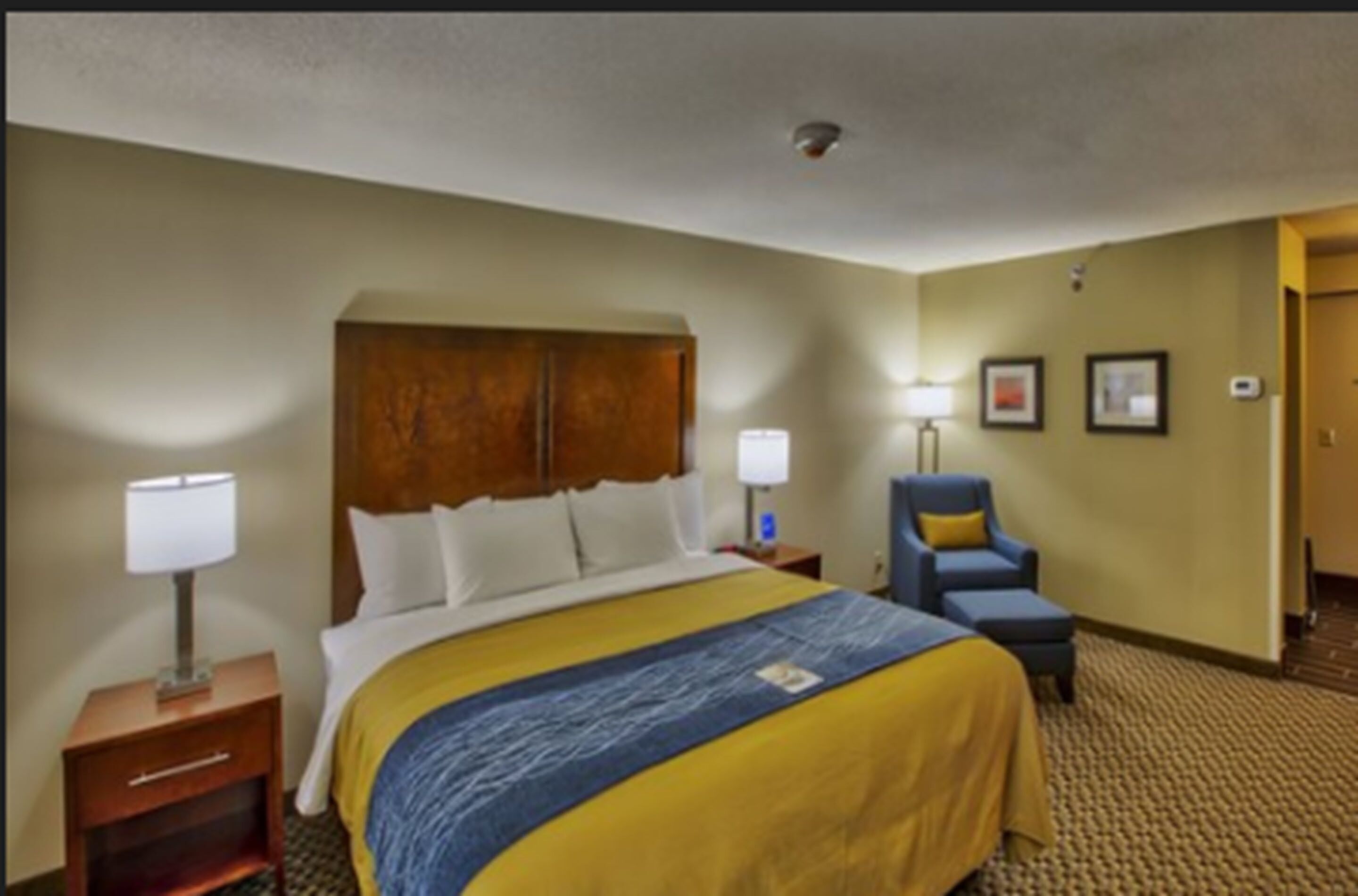 A hotel room with a large bed, a nightstand with a lamp, a chair, and a wall-mounted TV.