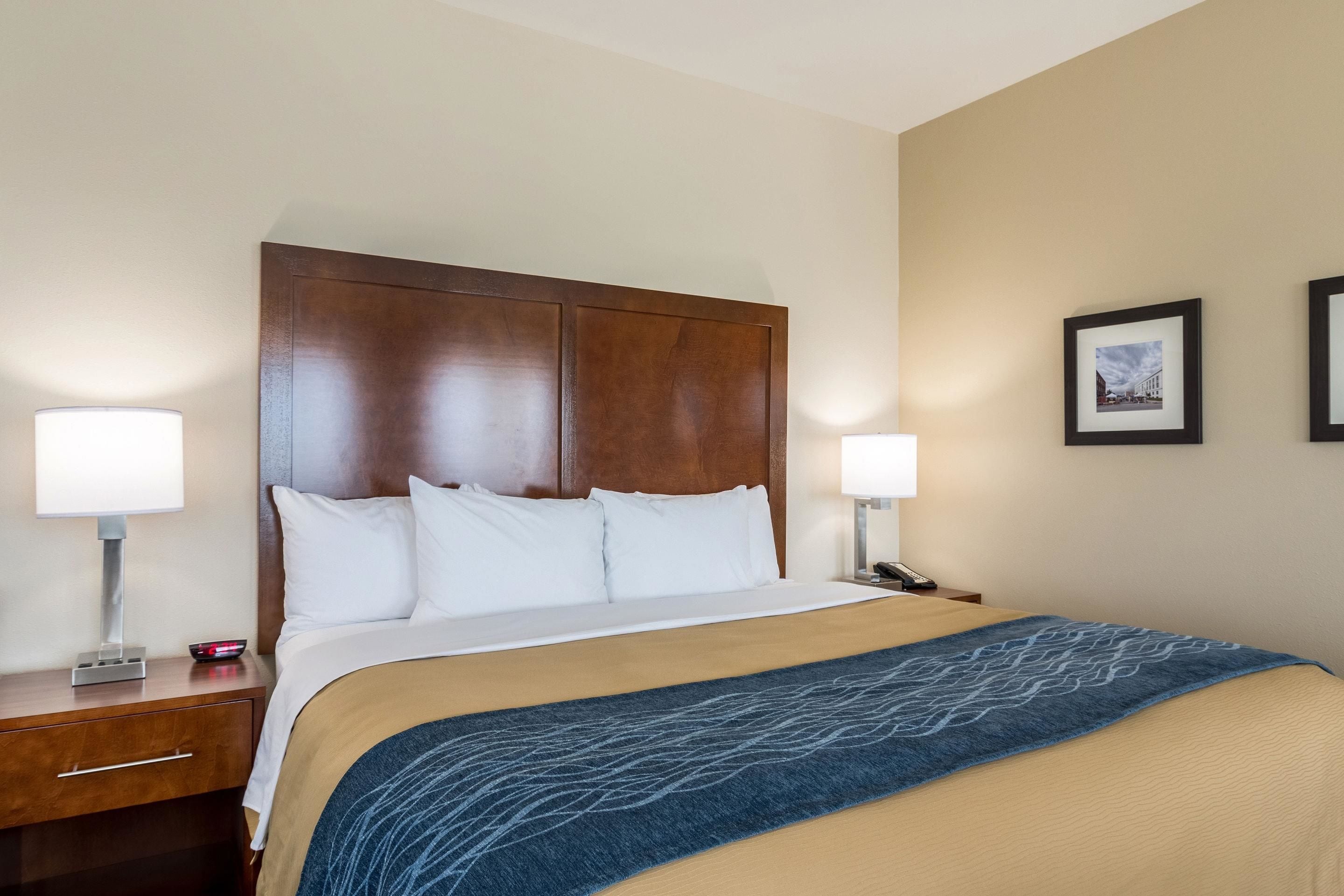 A hotel room with a large bed, wooden headboard, two bedside tables, and a nightstand.