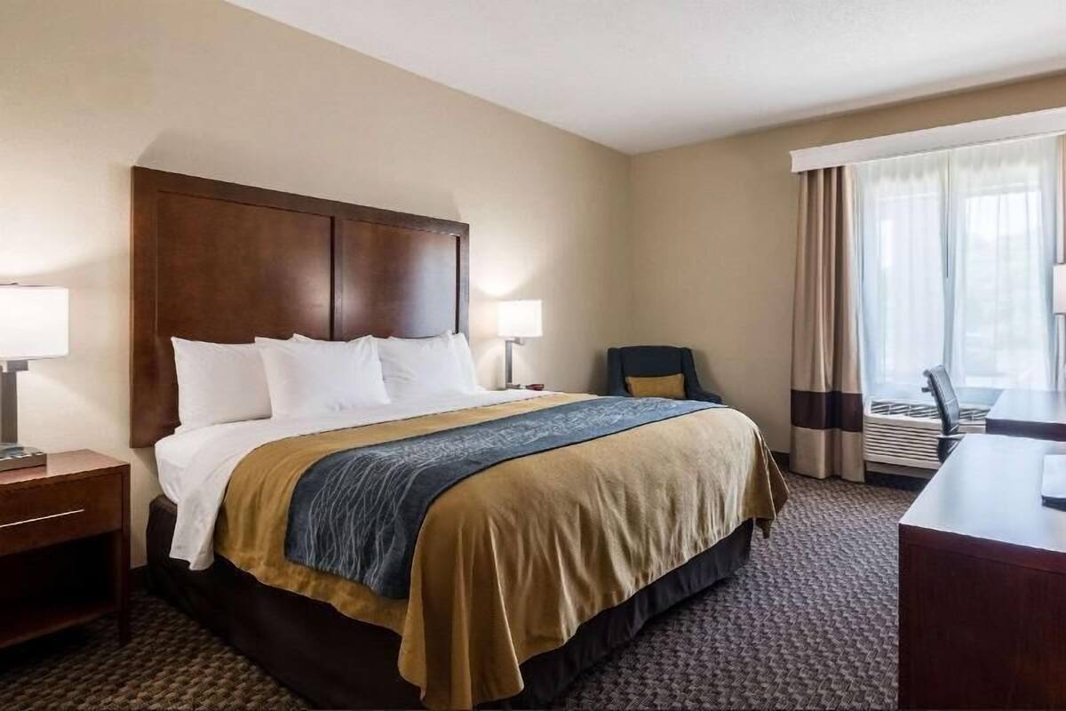 Une chambre d’hôtel avec un grand lit, un bureau, une chaise et une fenêtre avec des rideaux.