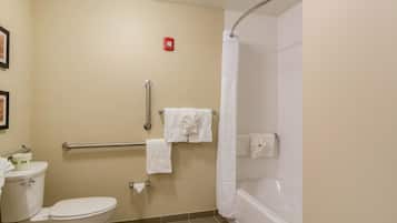 A bathroom with a toilet, a shower with a curtain, a handrail, and a towel rack with towels.