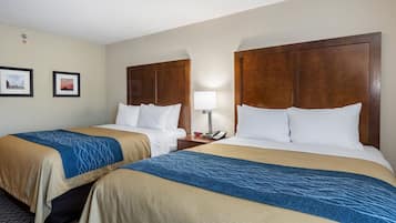 A hotel room with two beds, each with a wooden headboard, a bedside table with a lamp, and a framed picture on the wall.