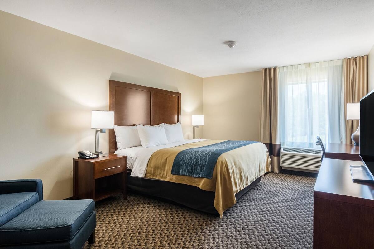 Une chambre d’hôtel avec un lit, des tables de chevet, un bureau, une chaise et une fenêtre avec des rideaux.