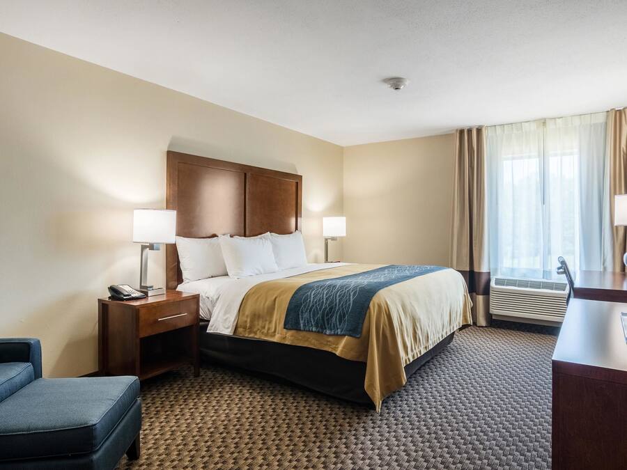 A hotel room with a bed, bedside tables, a desk, a chair, and a window with curtains.