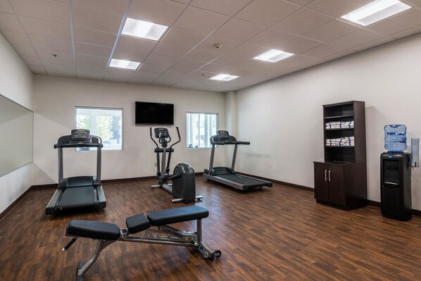 Un gimnasio con cintas de correr, elípticas y una banca.