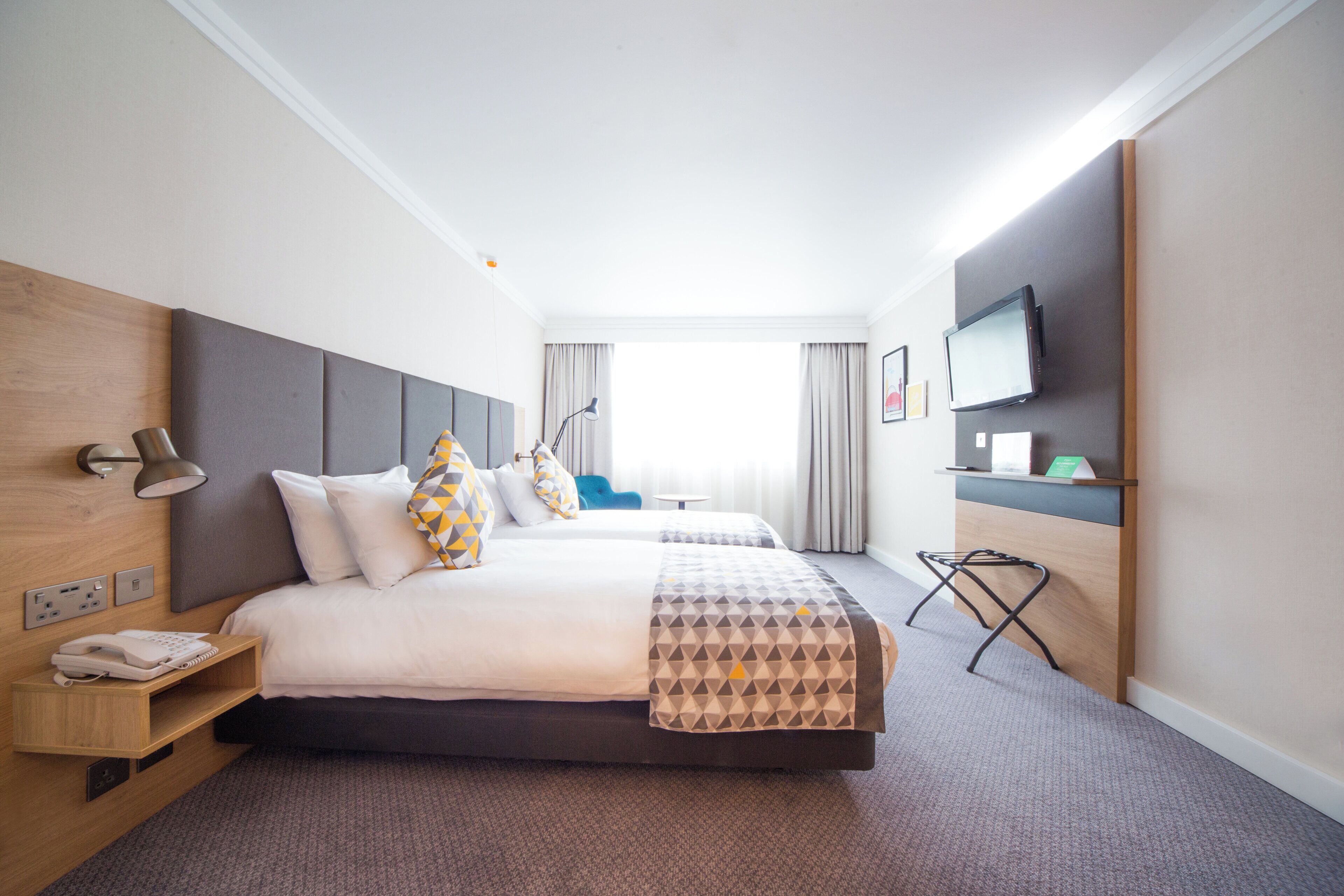 A hotel room with a bed, bedside lamp, telephone, and a television on the wall.