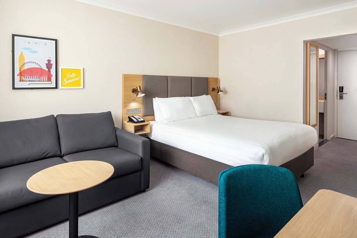 A hotel room with a bed, a sofa, a small table, and two wall-mounted lamps.