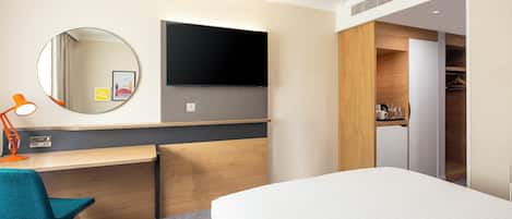 A hotel room with a bed, a desk with a chair, a TV mounted on the wall, and a closet.