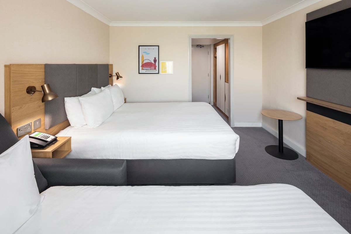 A hotel room with two beds, a TV, a desk with a lamp, and a small table.