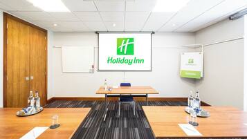 A conference room with a Holiday Inn logo on the screen, a whiteboard, and a welcome sign.
