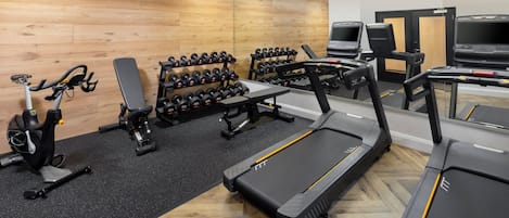 A gym with treadmills, stationary bikes, dumbbells, and weight benches.