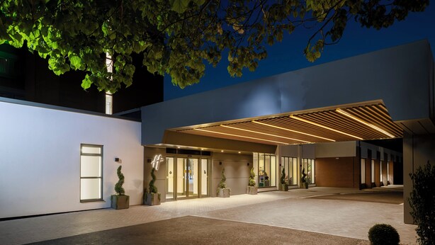 A modern building entrance with a covered walkway, glass doors, and potted plants. - Holiday Inn London-Gatwick Airport by IHG (Horley)