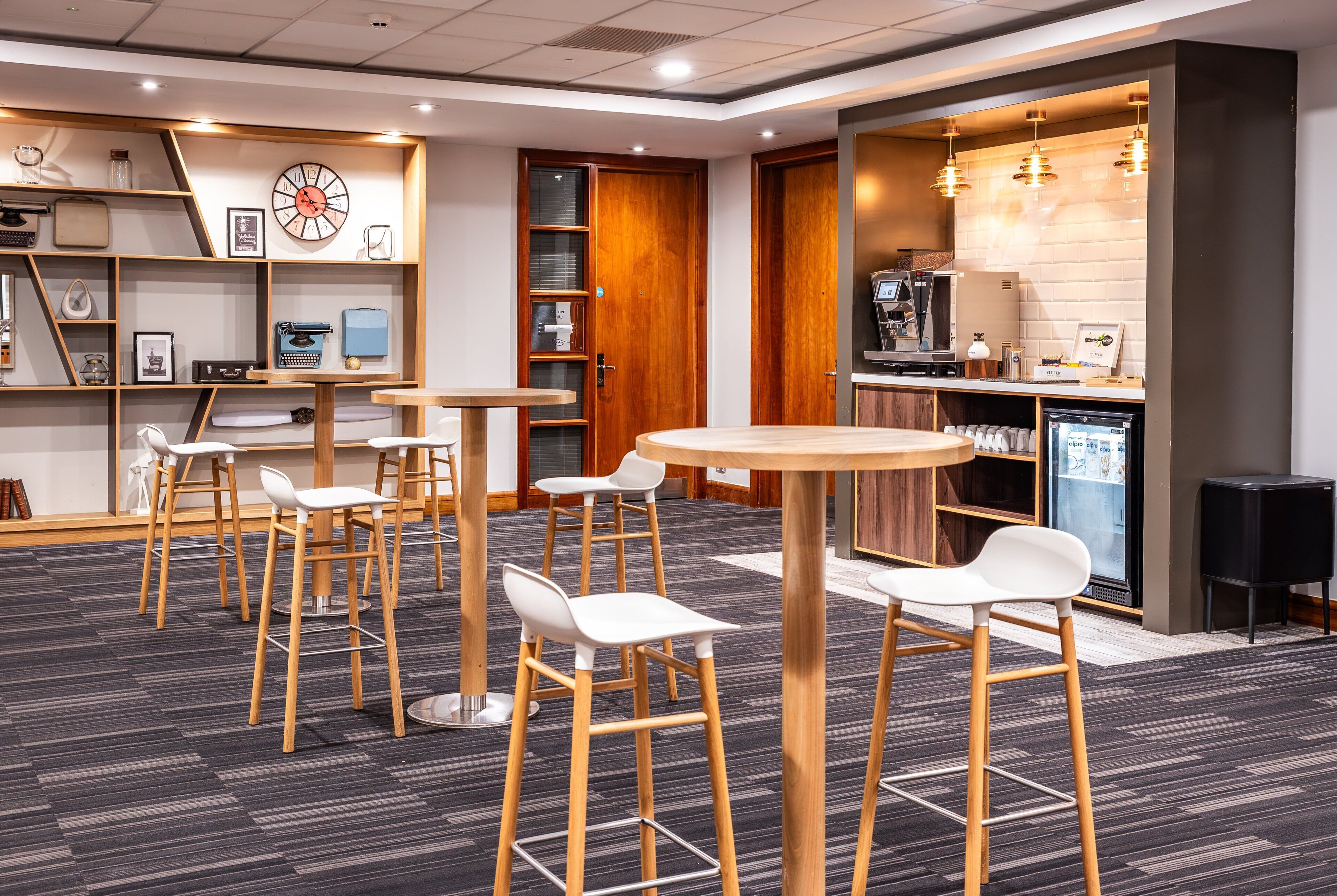 A modern bar area with wooden stools, a round table, and a coffee machine.