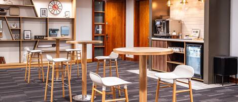 A modern bar area with wooden stools, a round table, and a coffee machine.