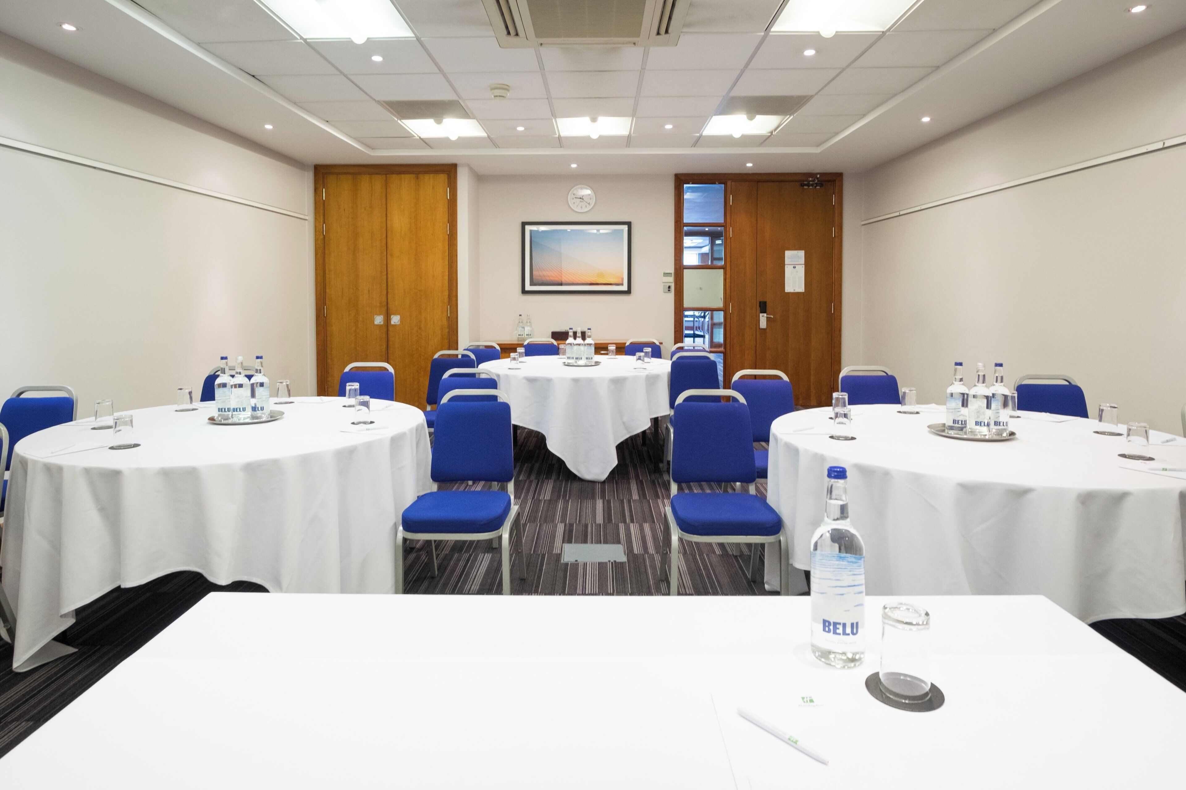 A conference room with round tables, blue chairs, and white tablecloths.