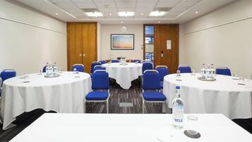 A conference room with round tables, blue chairs, and white tablecloths.