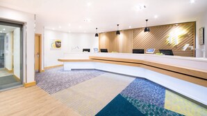 A modern reception area with a curved reception desk, multiple computer monitors, and pendant lighting. - Holiday Inn London-Gatwick Airport by IHG (Horley)