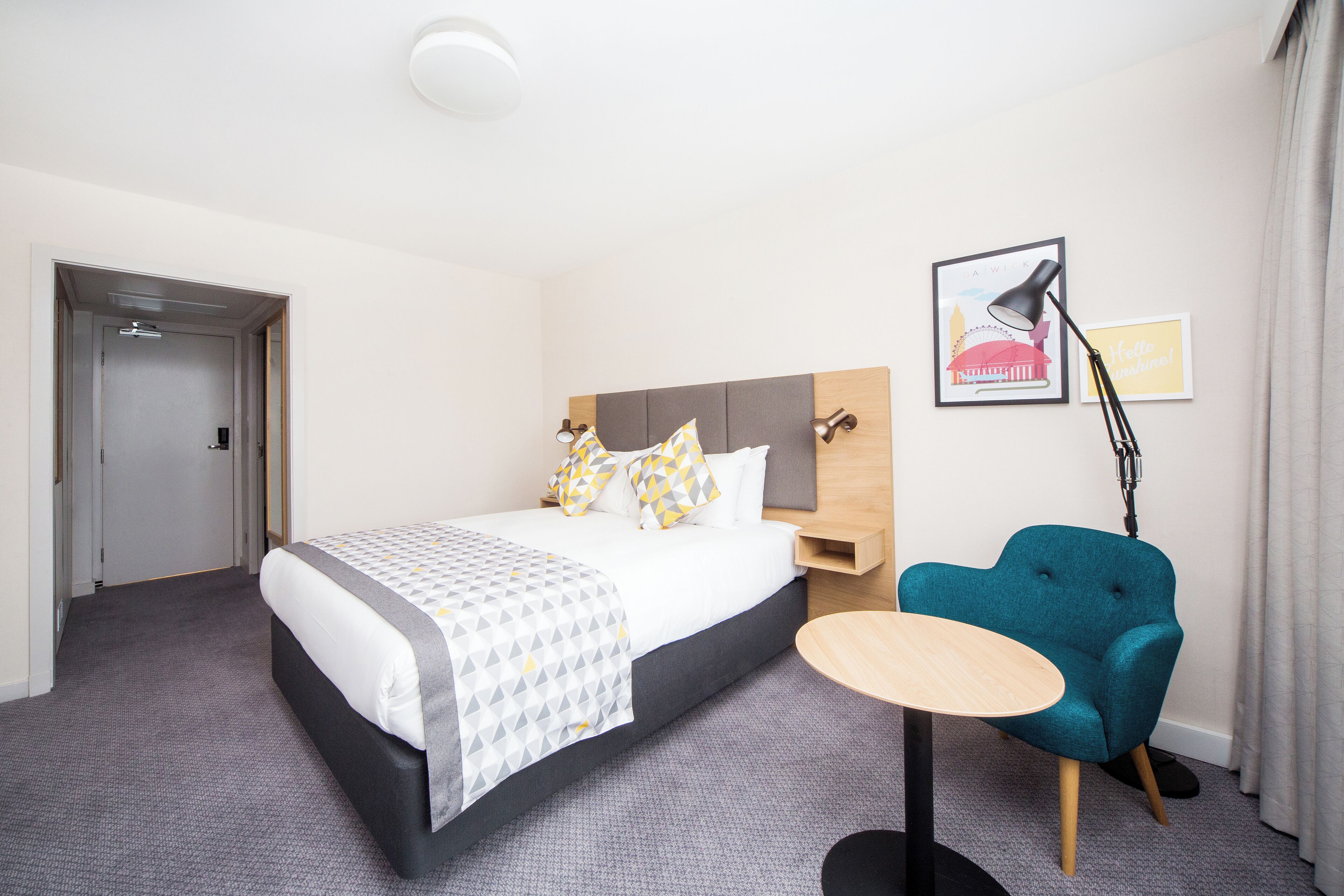 Une chambre d’hôtel comprenant un lit, une table de chevet, une chaise et une lampe fixée au mur.