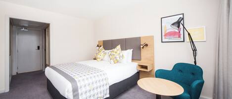 Une chambre d’hôtel comprenant un lit, une table de chevet, une chaise et une lampe fixée au mur.