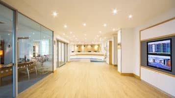 Un vestíbulo de hotel con mostrador de recepción, zona de estar y un panel informativo digital.