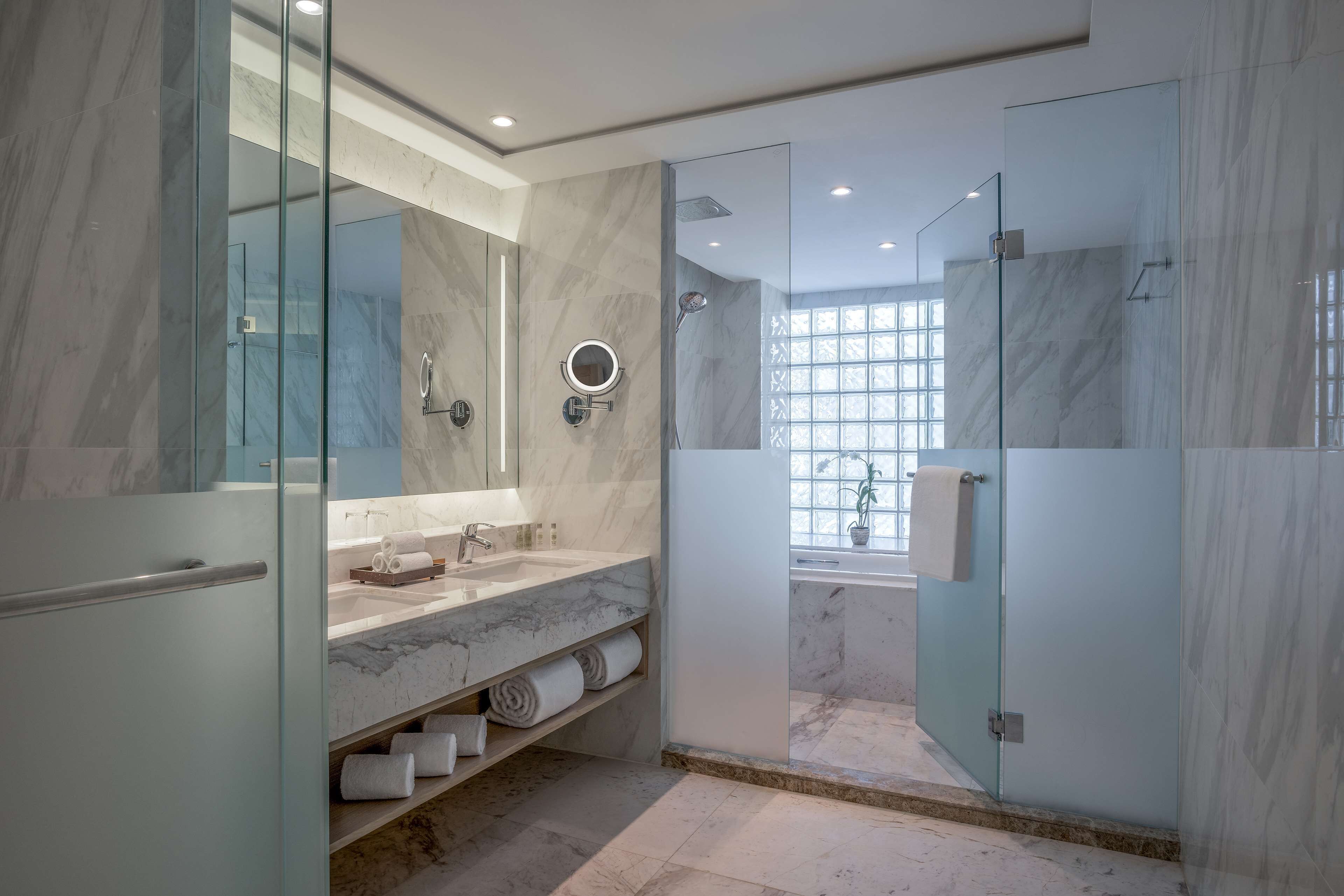 A modern bathroom with a marble vanity, glass shower enclosure, and a large mirror.