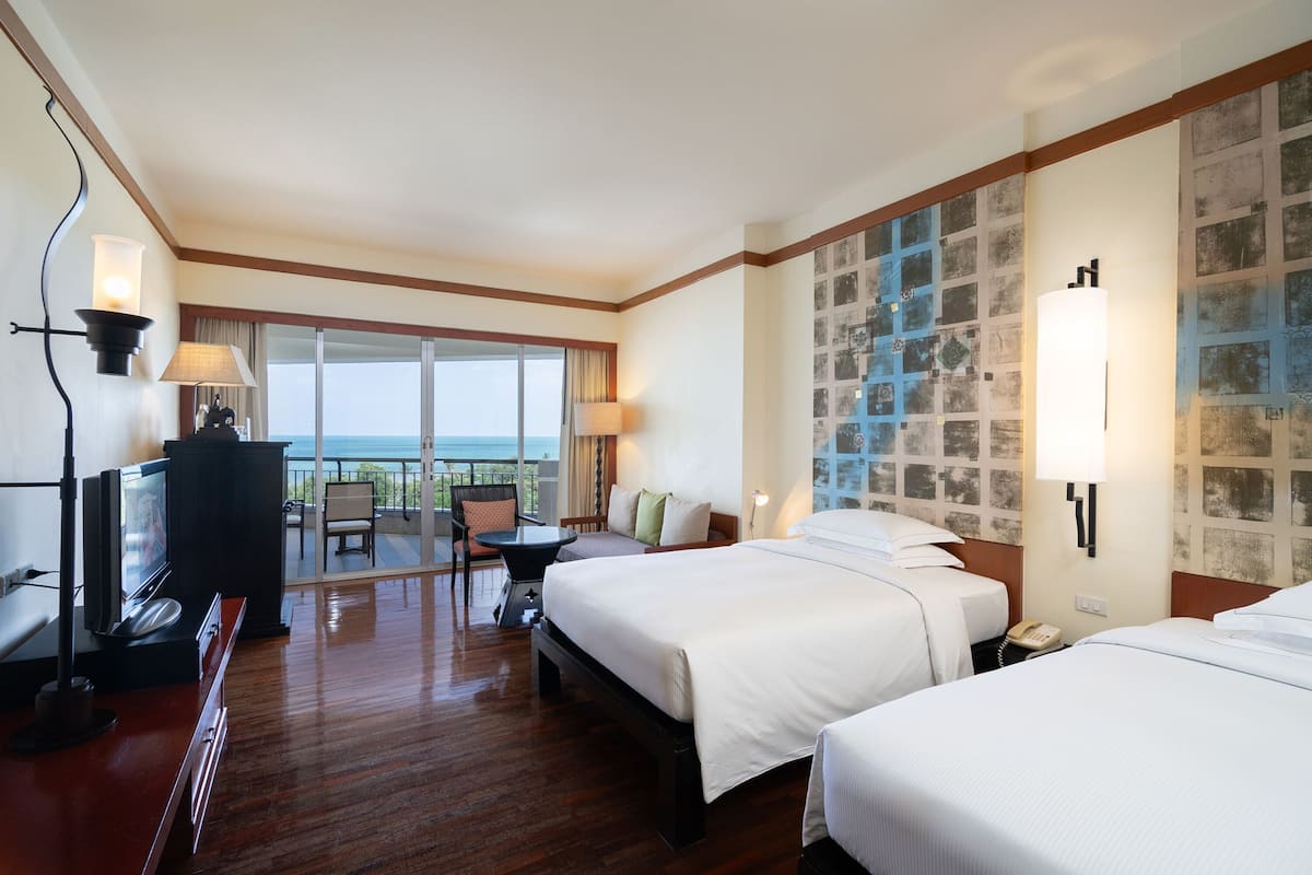 Hotelkamer met twee bedden, een televisie, een bureau met stoel en een balkon met uitzicht op zee.