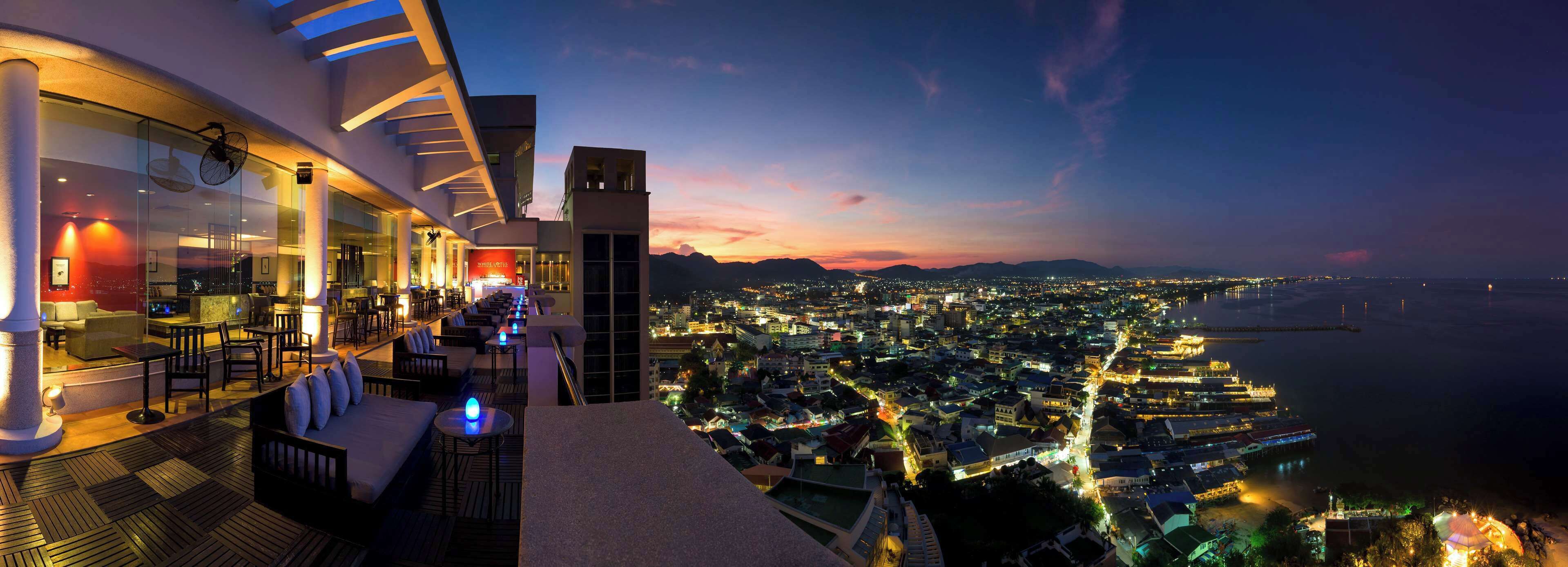 Ein modernes Hotel mit Dachterrasse und Blick auf die Stadt bei Einbruch der Dunkelheit.