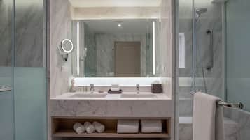 Un baño moderno con encimeras de mármol, lavamanos doble, ducha con mampara de vidrio y estante empotrado con toallas.