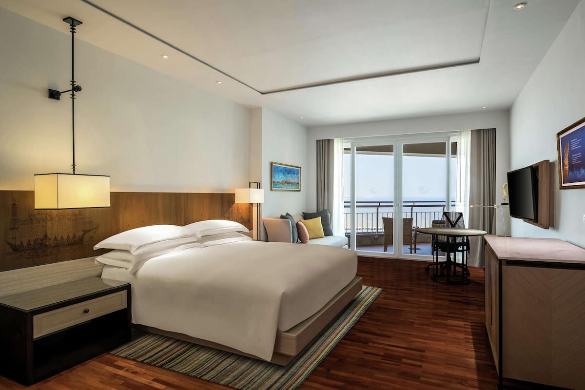 Een hotelkamer met een groot bed, een bureau met lamp, een zithoek met tafel en stoelen, en een aan de muur bevestigde televisie.