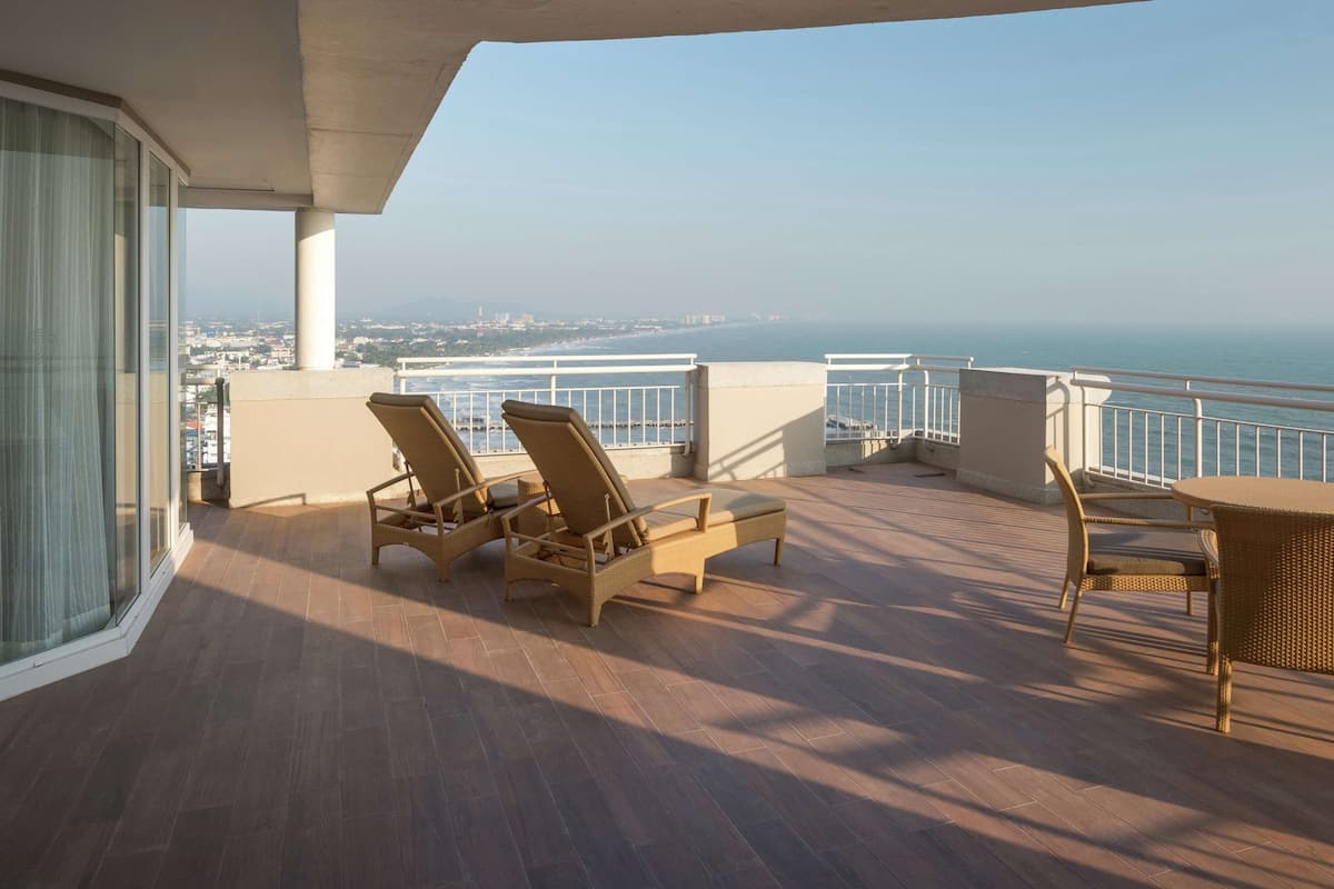 Een balkon met rieten meubilair, een plafondventilator en uitzicht op zee.
