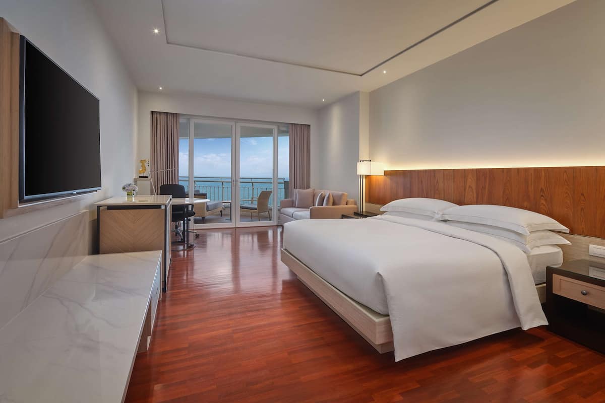 Een moderne hotelkamer met een groot bed, een bureau en uitzicht op zee door de glazen deuren.
