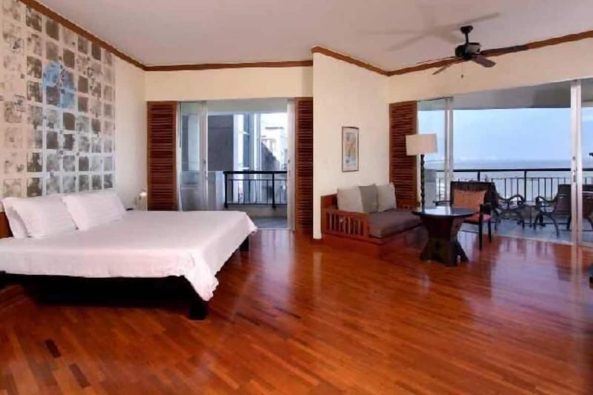 Een hotelkamer met een bed, een balkon met een tafel en stoelen, en uitzicht op de oceaan.