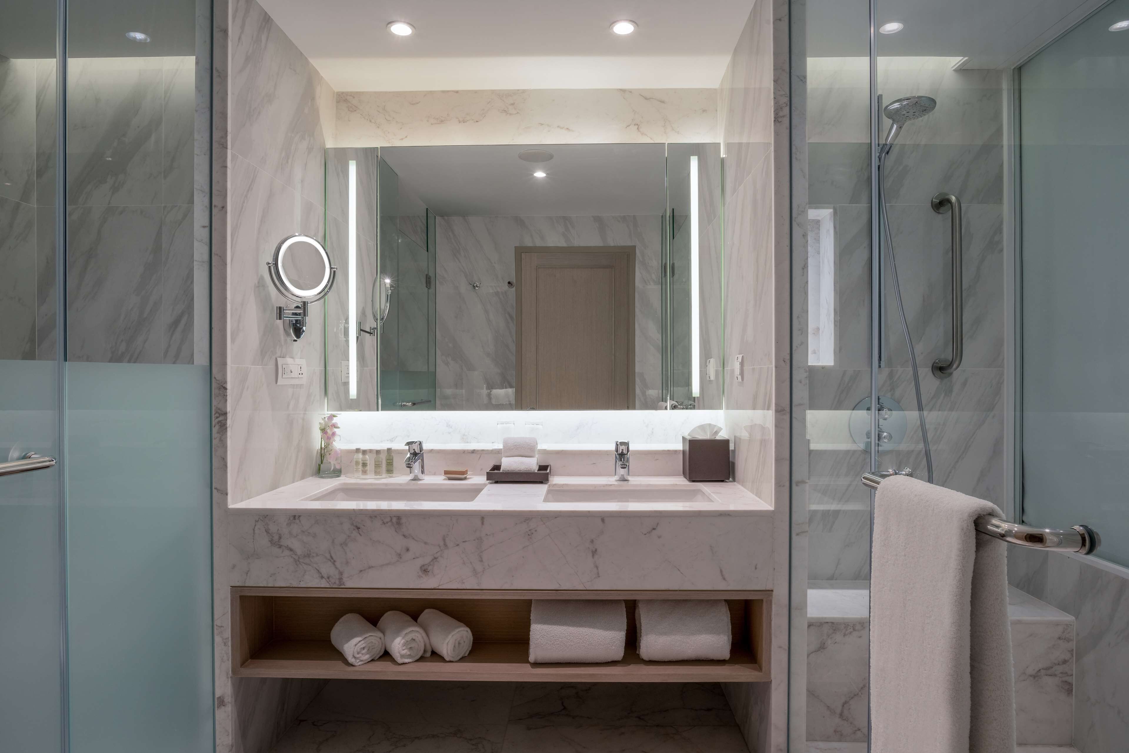 Een moderne badkamer met een grote spiegel, dubbele wastafels en een douche met glazen wanden.