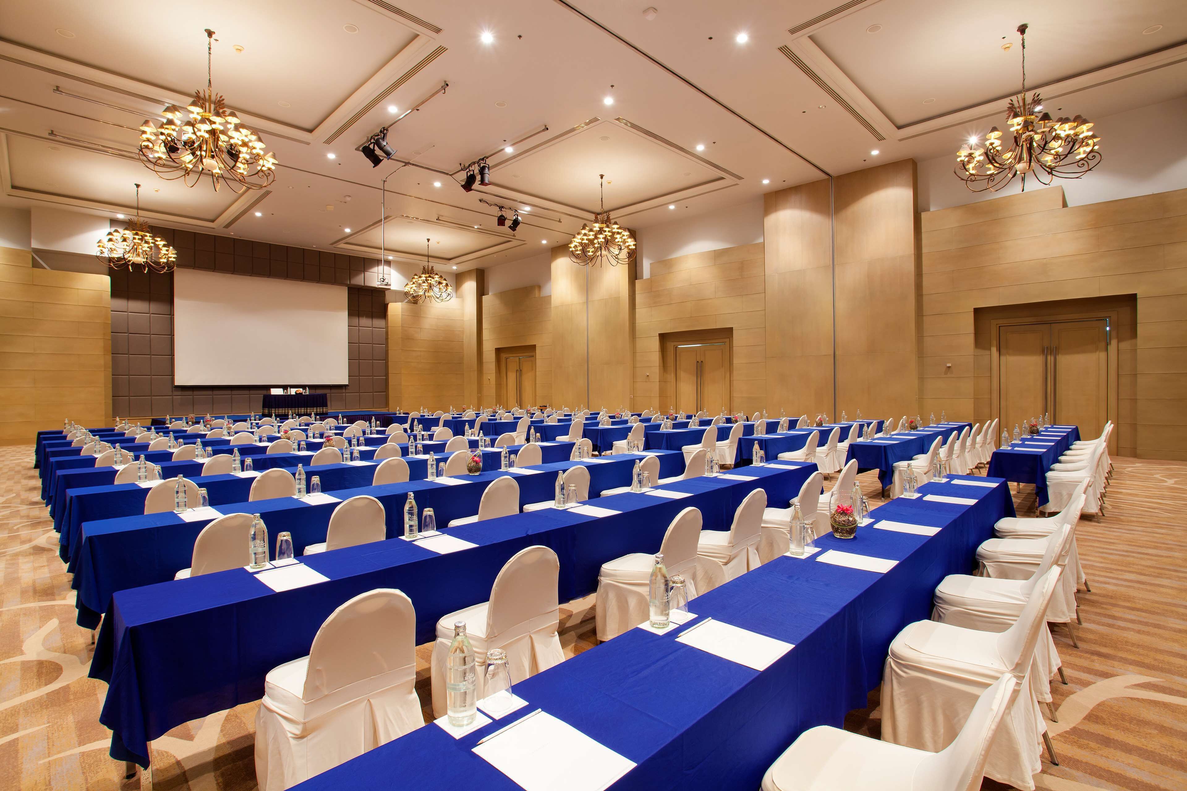 Un salón de conferencias con filas de mesas, sillas y una gran pantalla al frente.