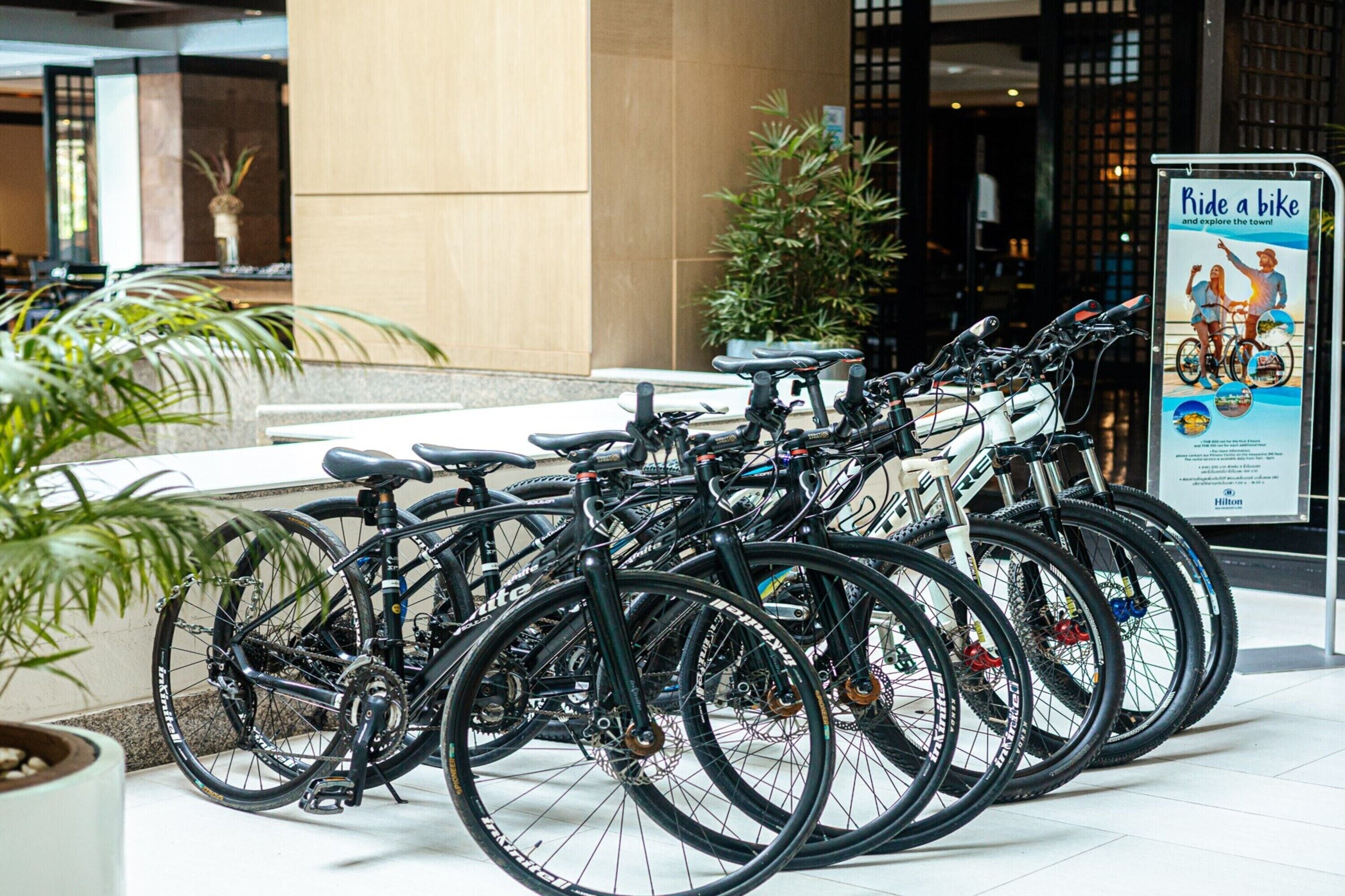 A row of bicycles parked in a hotel lobby with a sign promoting bike rentals.