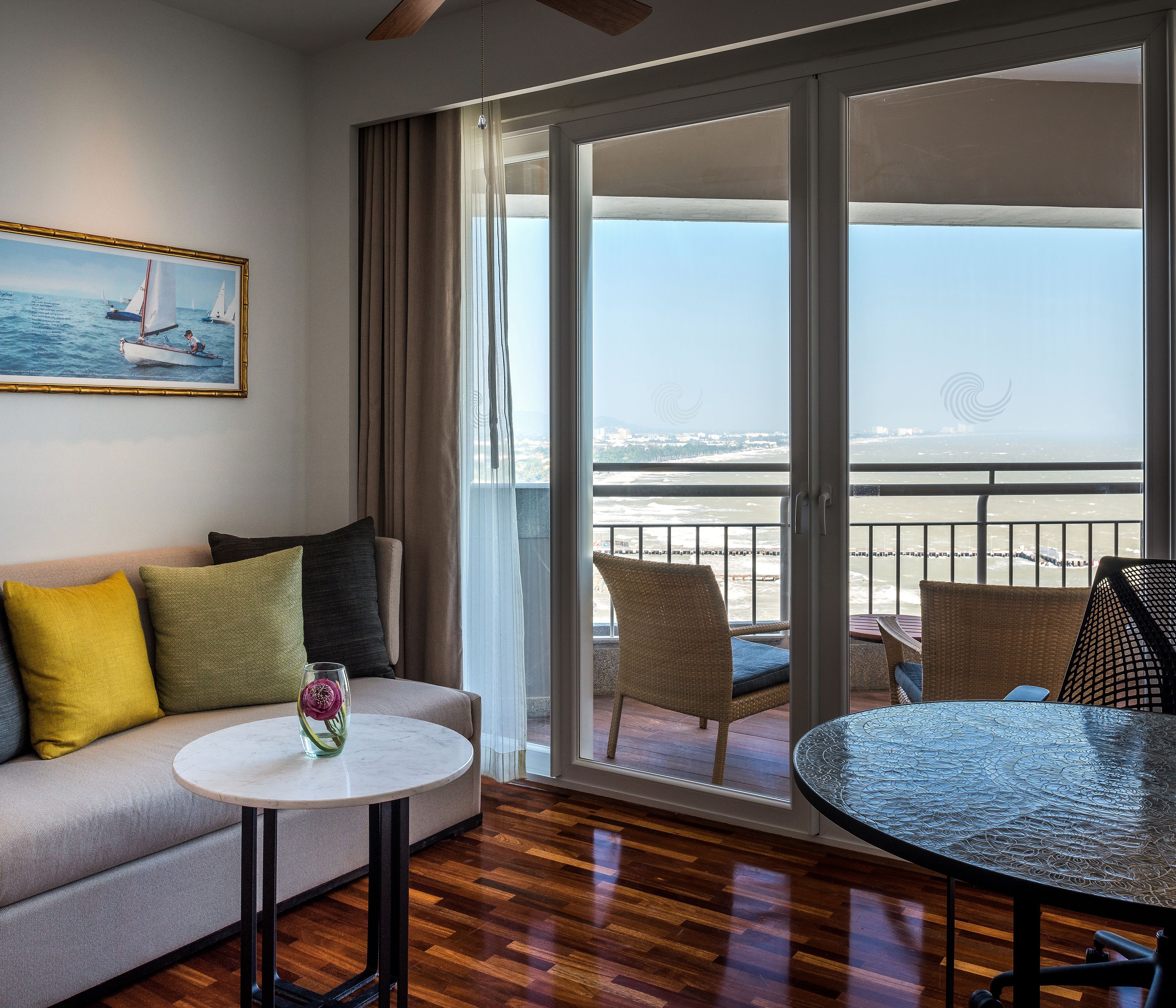 A room with a sofa, a small table, and a balcony with wicker chairs and a glass table.