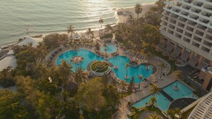 Un resort con varias piscinas, palmeras y vistas a la playa.
